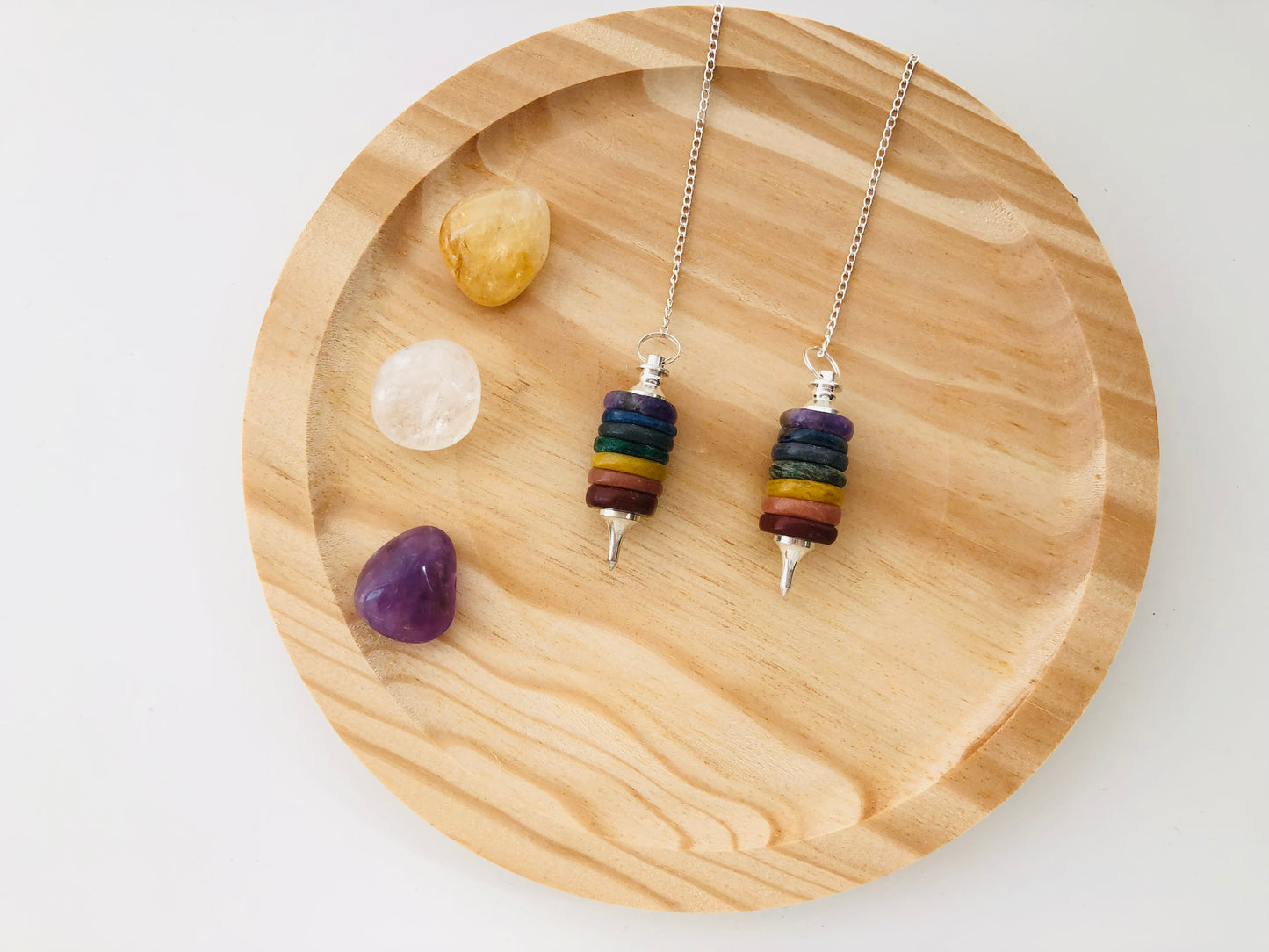 Péndulo artesanal compuesto por siete gemas de colores representando los chakras, con punta facetada y cadena.