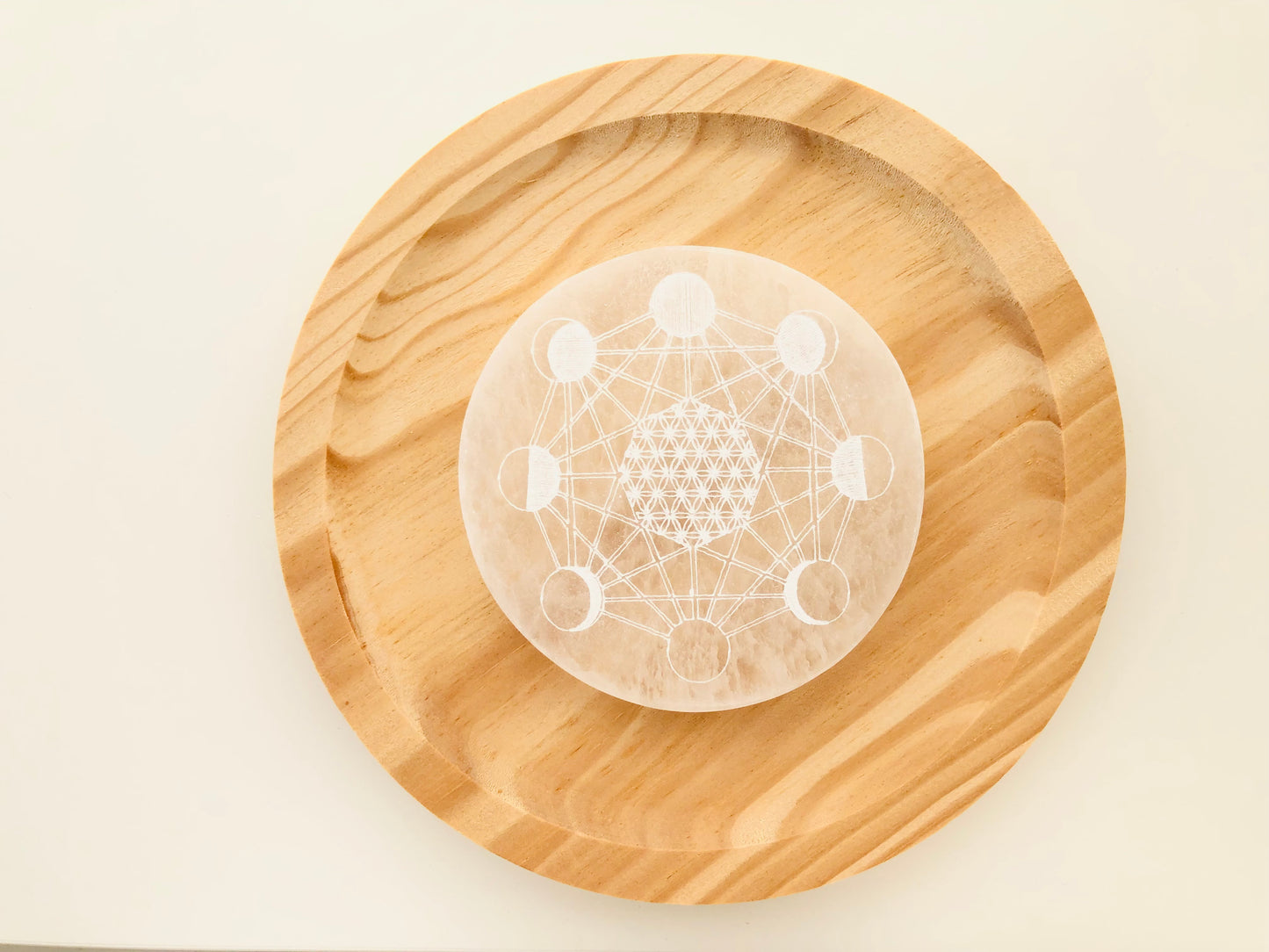 Plato circular de selenita blanca natural con grabado de las fases lunares, diseñado como base para limpiar y cargar energéticamente otros cristales.
