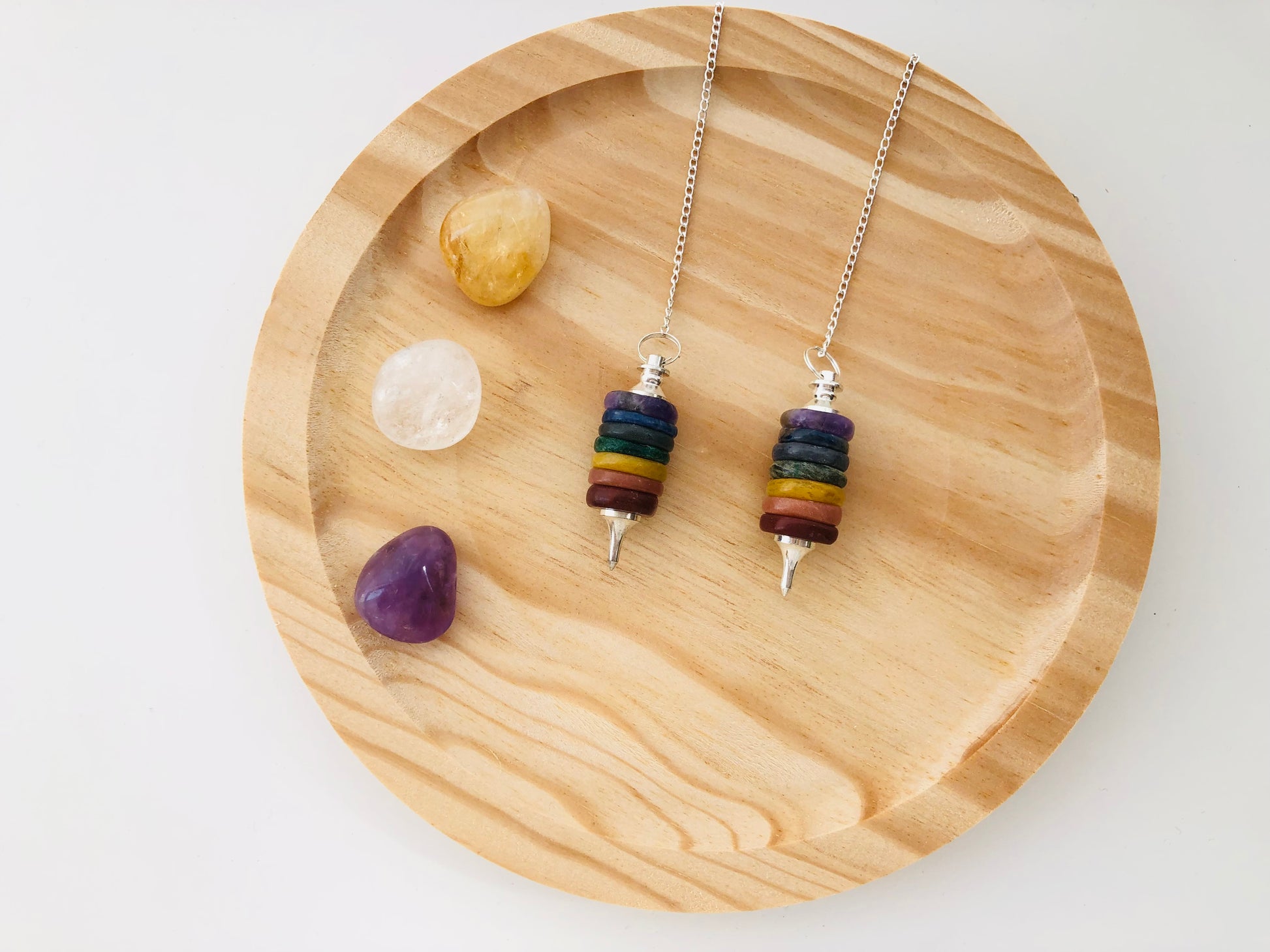 Péndulo artesanal compuesto por siete gemas de colores representando los chakras, con punta facetada y cadena.