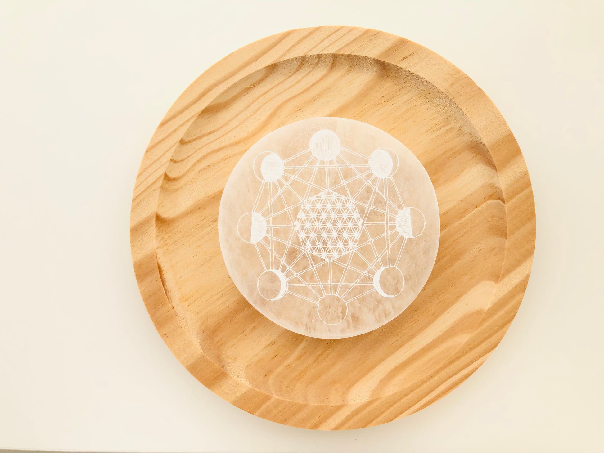 Plato circular de selenita blanca natural con grabado de las fases lunares, diseñado como base para limpiar y cargar energéticamente otros cristales.