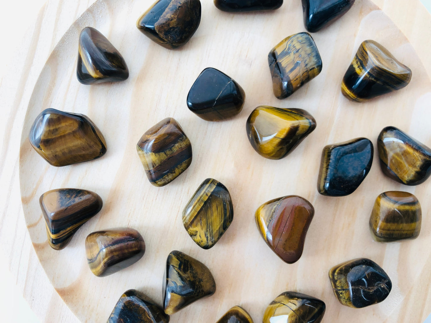 Piedra de ojo de tigre pulida de forma redondeada, mostrando bandas paralelas en tonos café, ocre y vetas doradas brillantes que reflejan la luz.