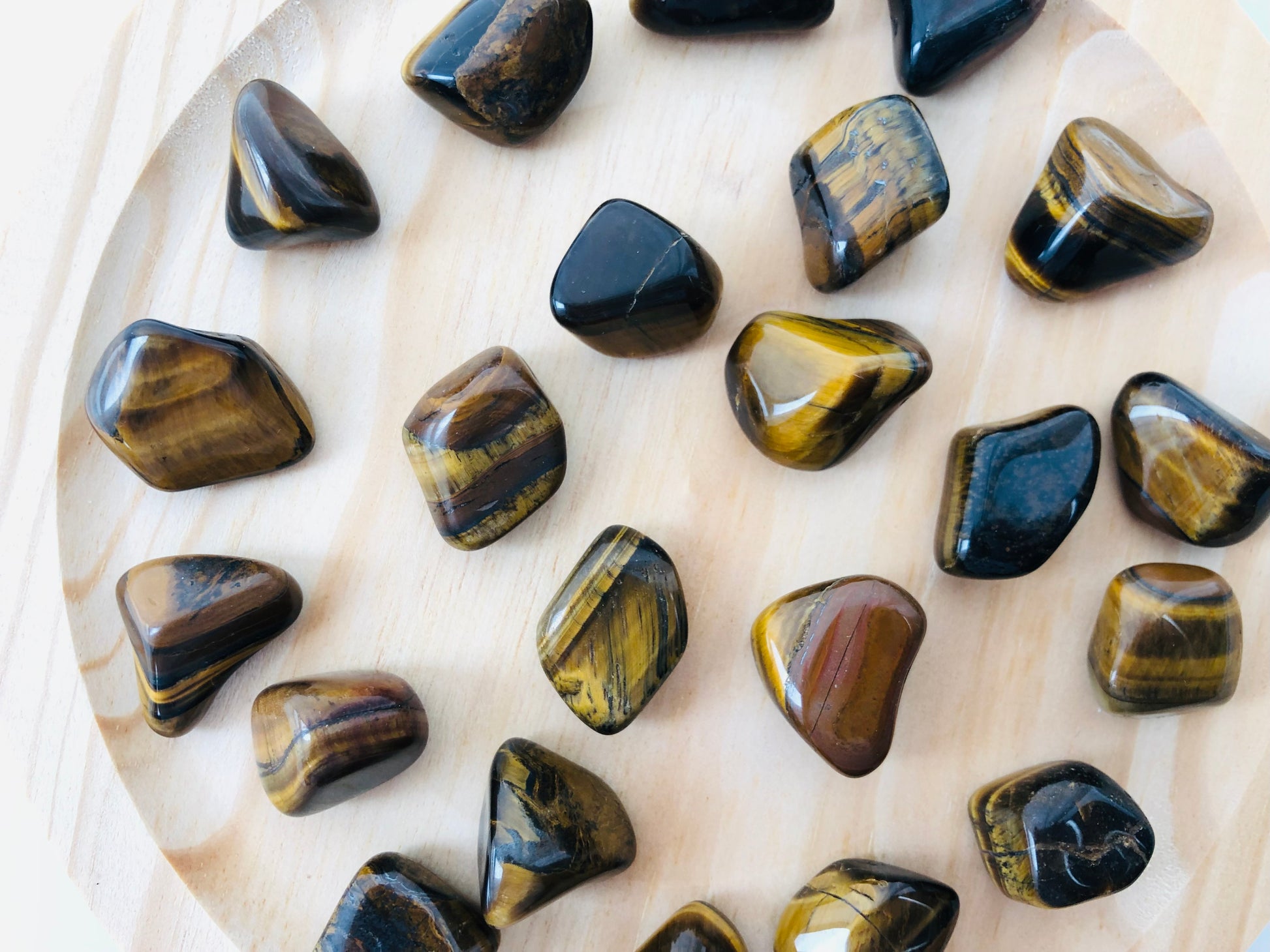 Piedra de ojo de tigre pulida de forma redondeada, mostrando bandas paralelas en tonos café, ocre y vetas doradas brillantes que reflejan la luz.