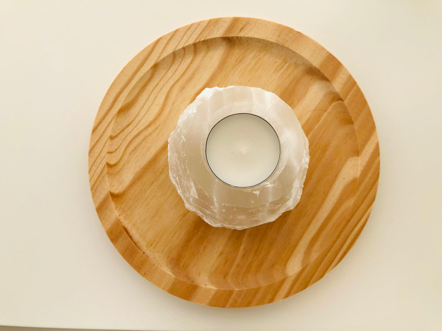 Portavelas cilíndrico de selenita blanca natural con superficie pulida y fibras traslúcidas, diseñado para sostener una vela pequeña que ilumina el mineral desde el interior.