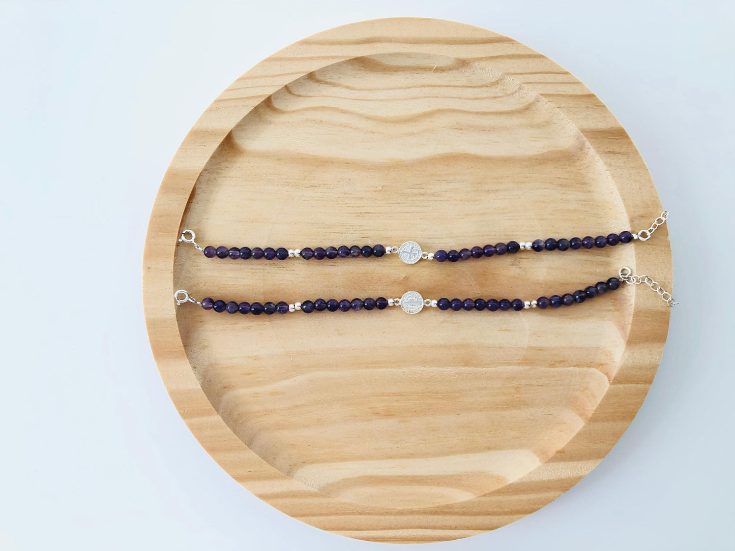 Detalle de pulsera de plata con piedras de amatista color violeta intenso y dije de San Benito, ideal para regalo especial.