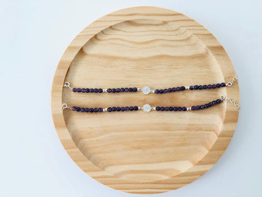 Detalle de pulsera de plata con piedras de amatista color violeta intenso y dije de San Benito, ideal para regalo especial.