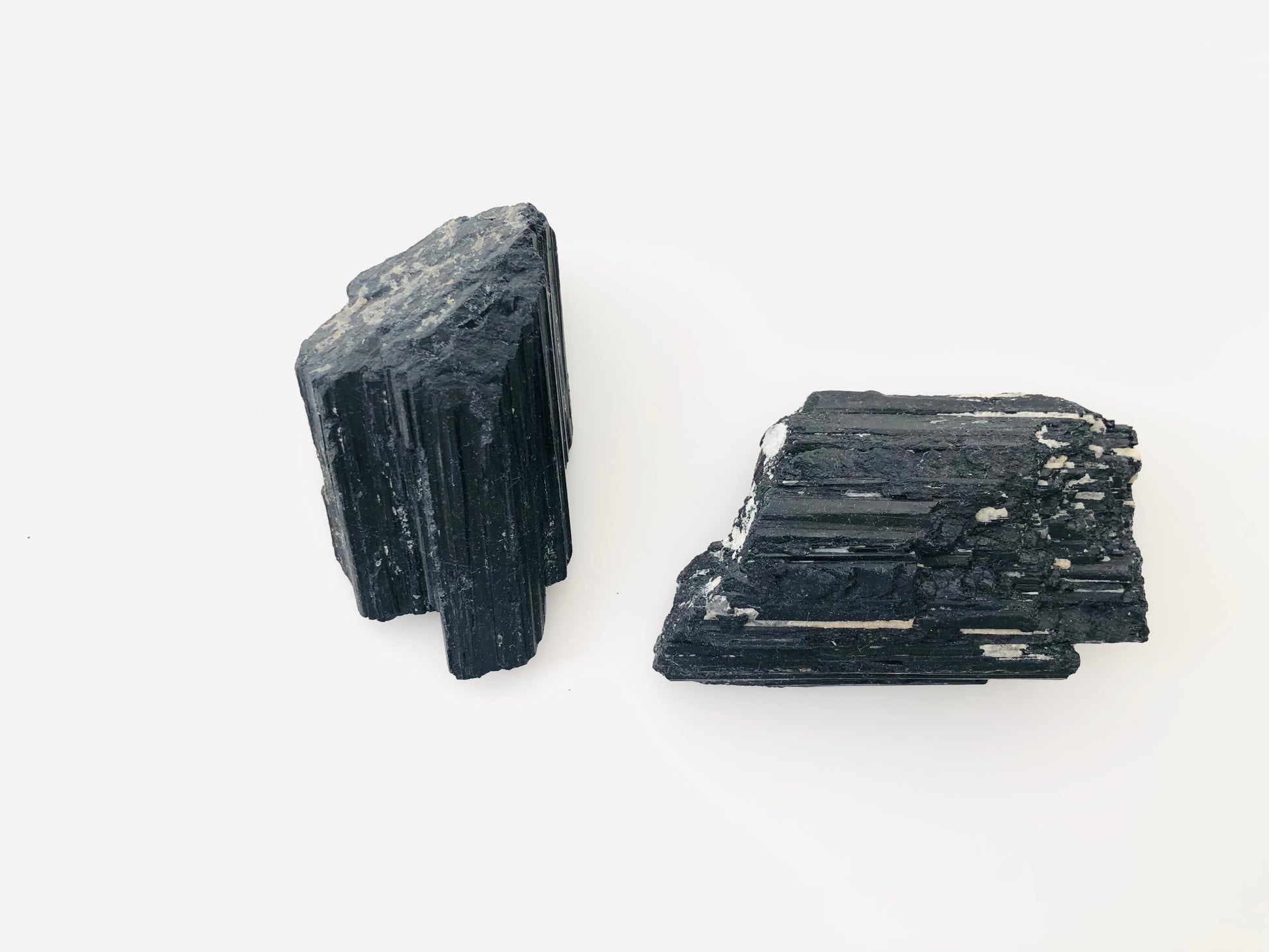 Cristal de turmalina negra natural en estado bruto con formación tipo catedral, mostrando sus características estrías verticales paralelas y una textura mineral opaca y robusta.