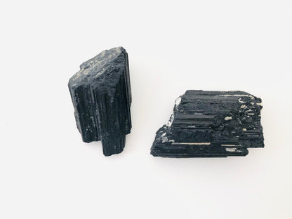 Cristal de turmalina negra natural en estado bruto con formación tipo catedral, mostrando sus características estrías verticales paralelas y una textura mineral opaca y robusta.